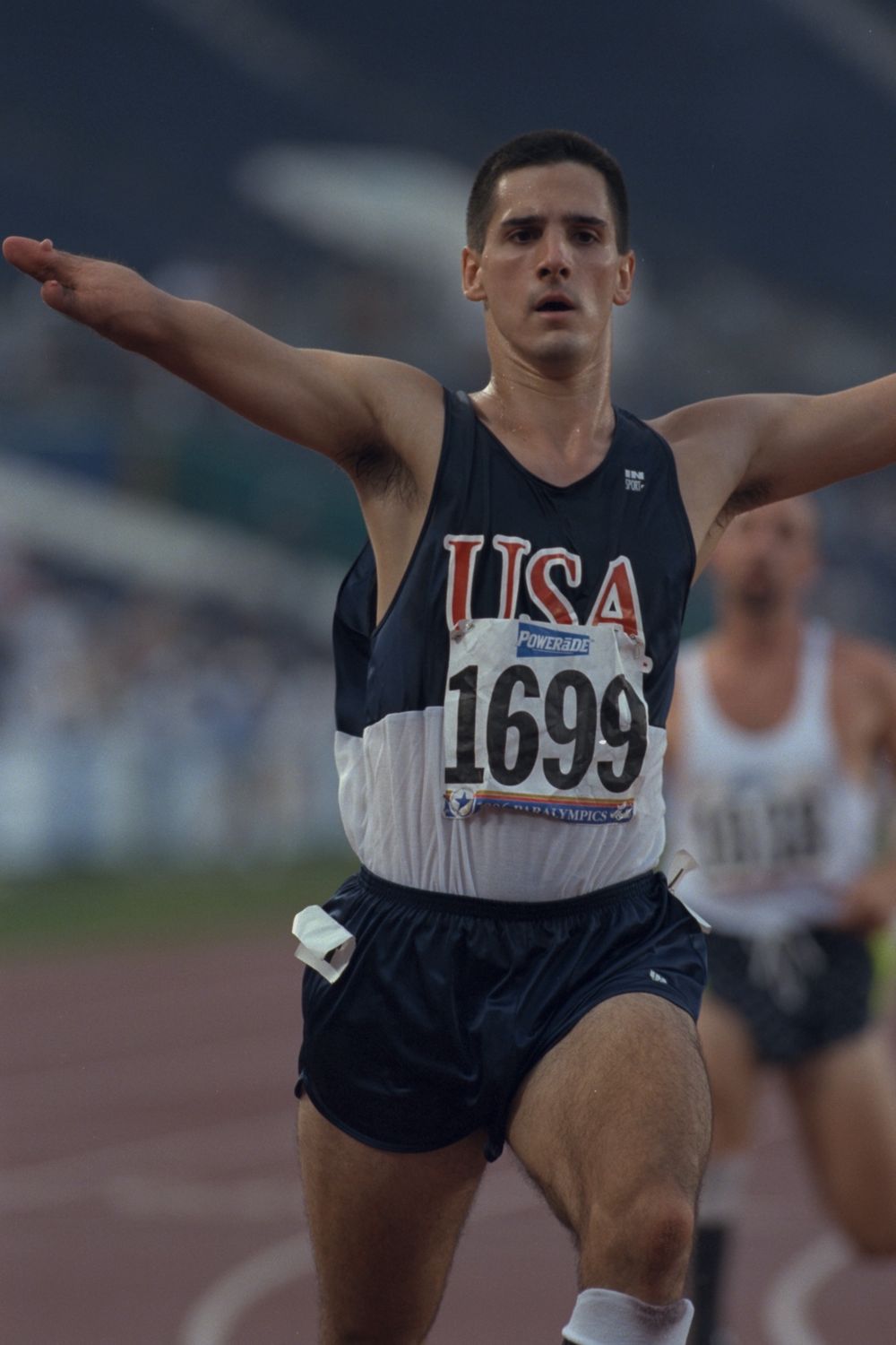 Tony Volpentest slowing after the line, arms still wide, another runner behind him