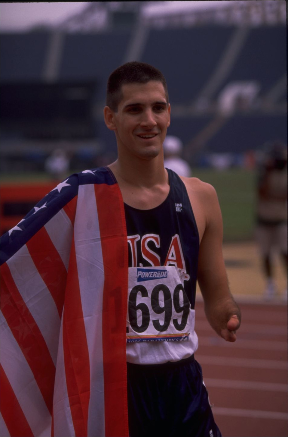 Tony Volpentest walking on the track with a US flag draped across his front
