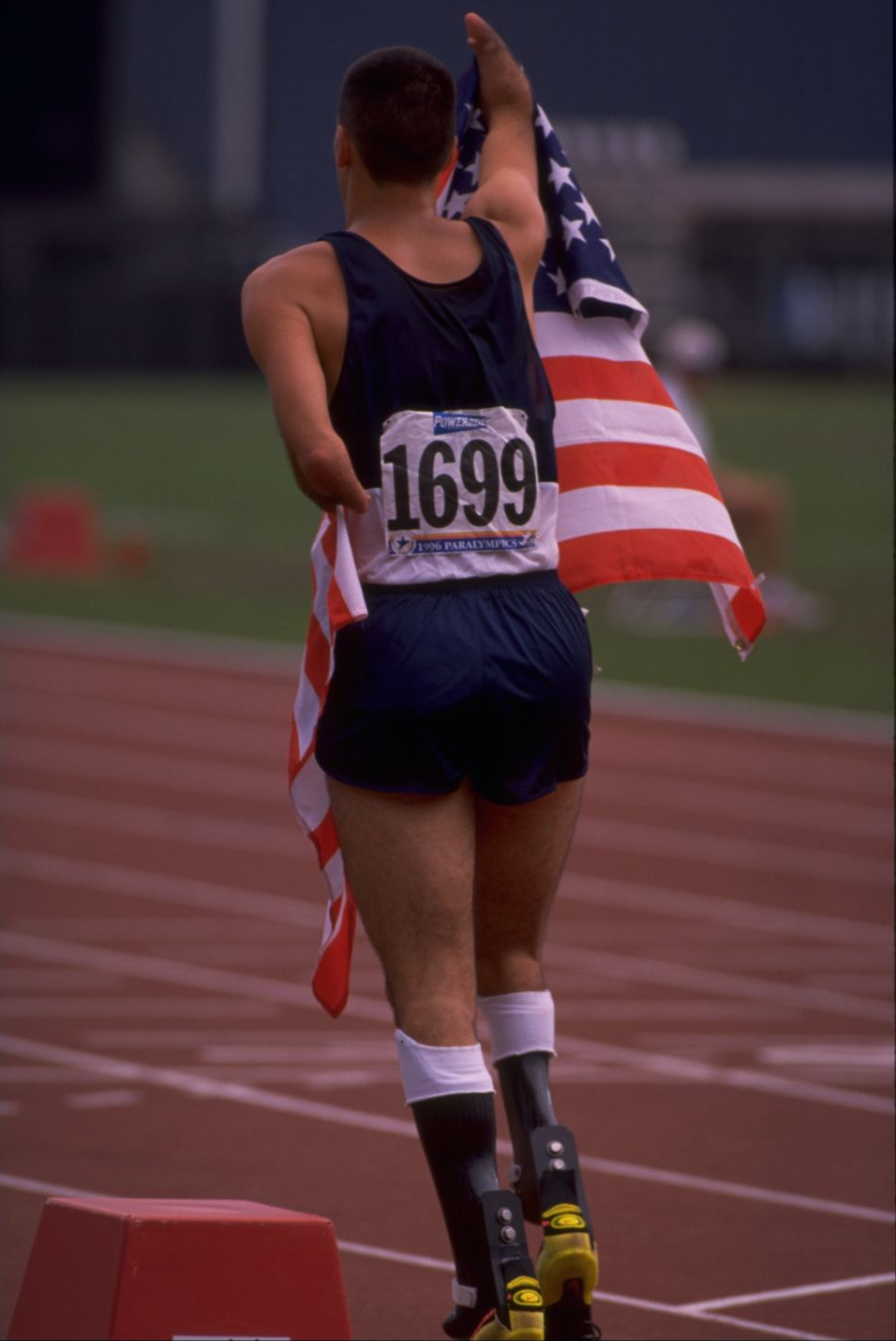 Tony Volpentest from behind, walking the track trailing a US flag