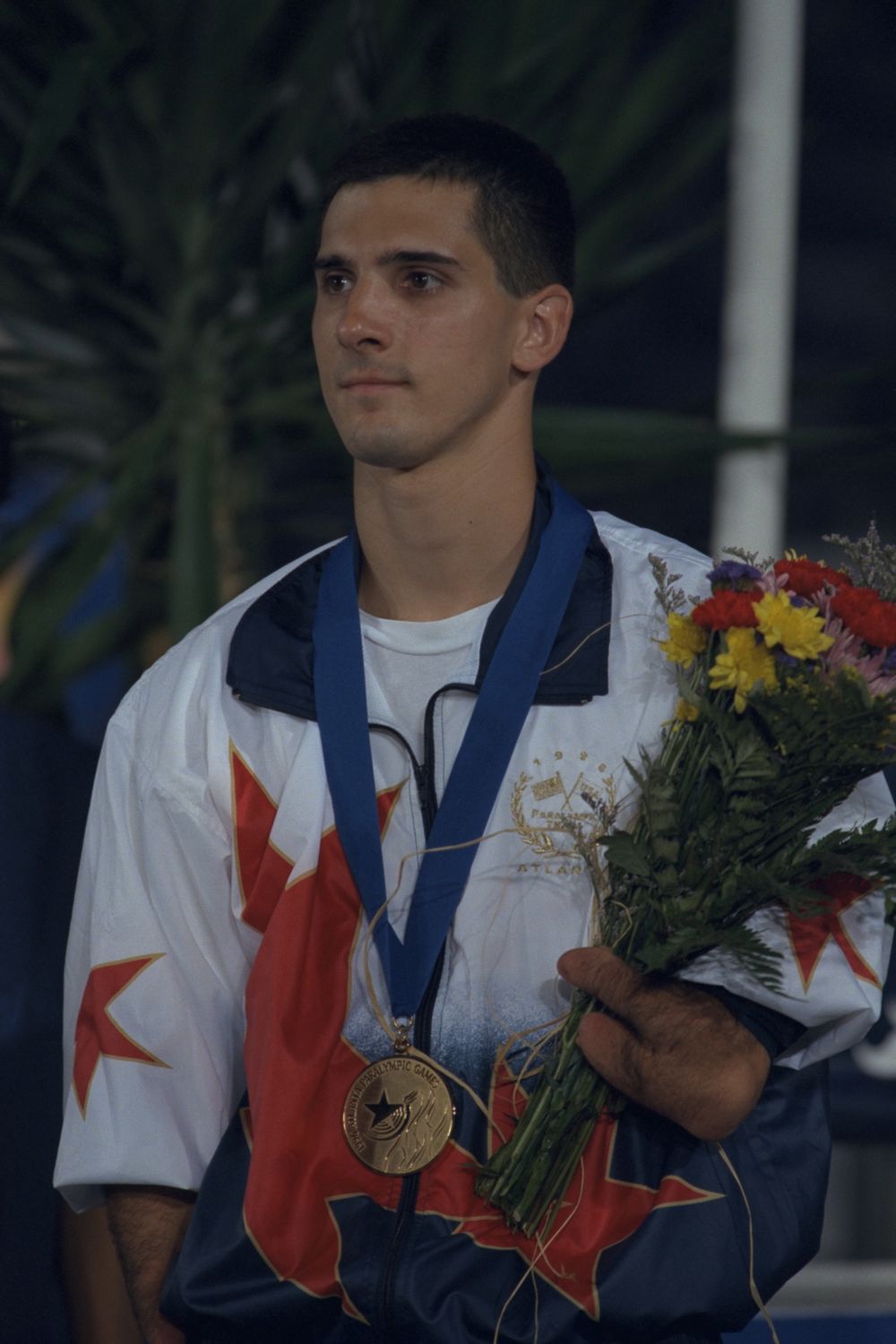 Tony Volpentest in a Team USA jacket with a gold medal on a blue ribbon and a bouquet, looking off camera