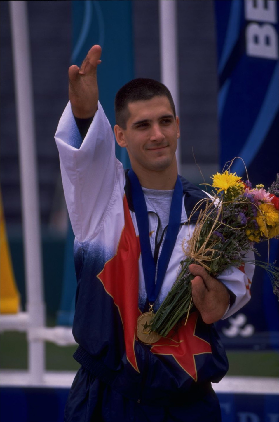 Tony Volpentest raising an arm, medal and bouquet held in the other