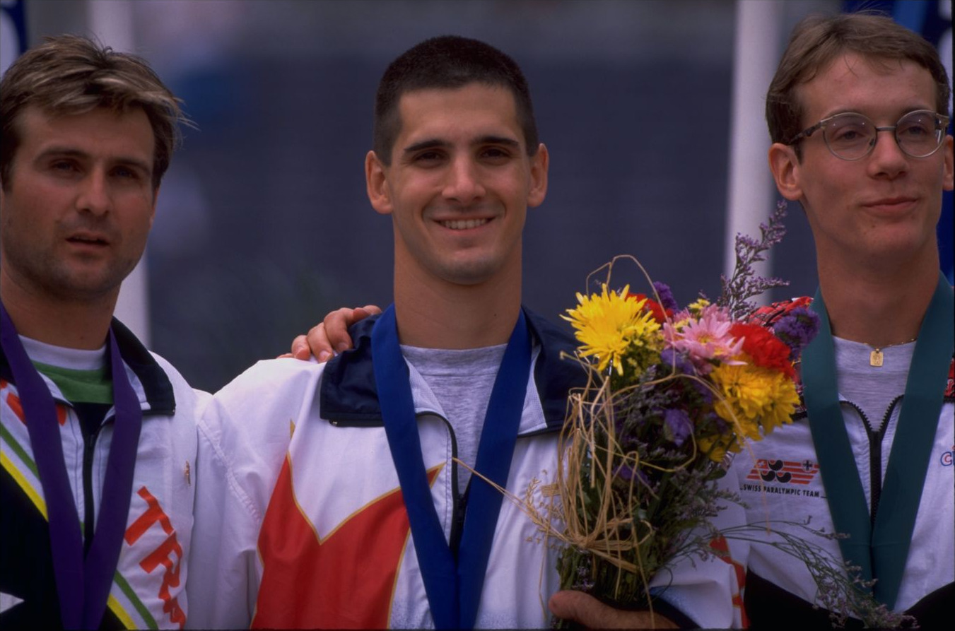 Tony Volpentest smiling between two other medalists, one hand on his shoulder