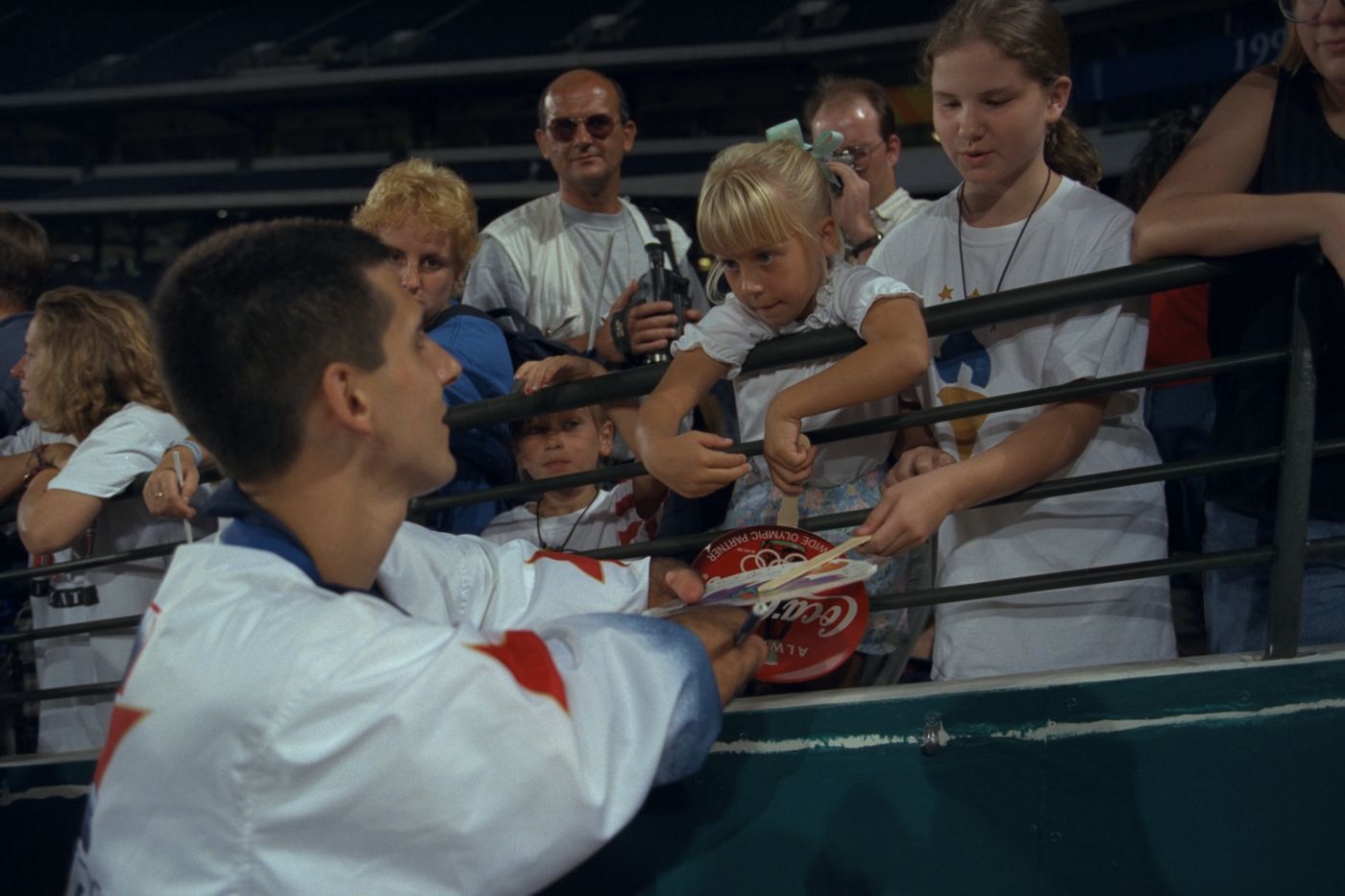 Tony Volpentest signing an autograph for a young girl leaning over the trackside rail
