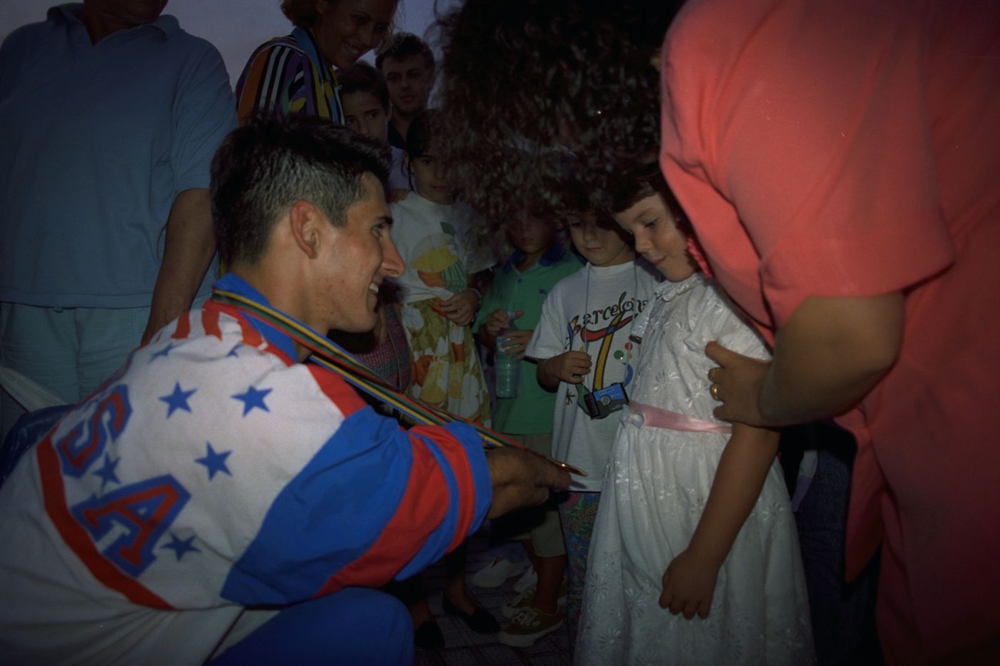 Tony Volpentest crouching to show his medal to a young girl in a white dress, Barcelona 1992