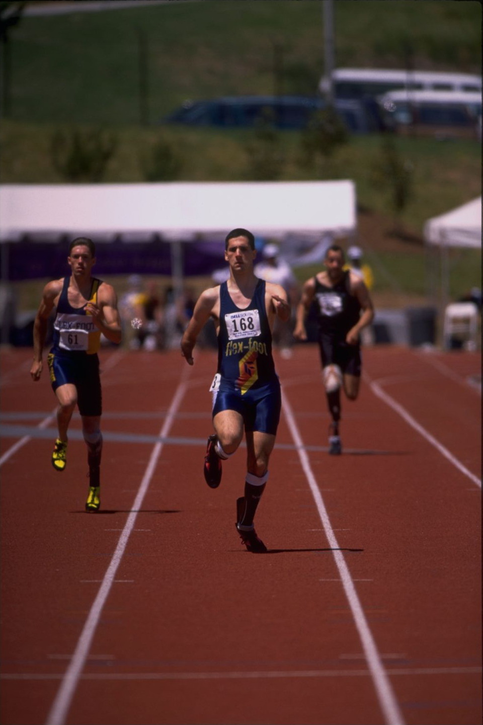 Tony Volpentest in a flex-foot singlet, bib 168, leading two runners down the straight