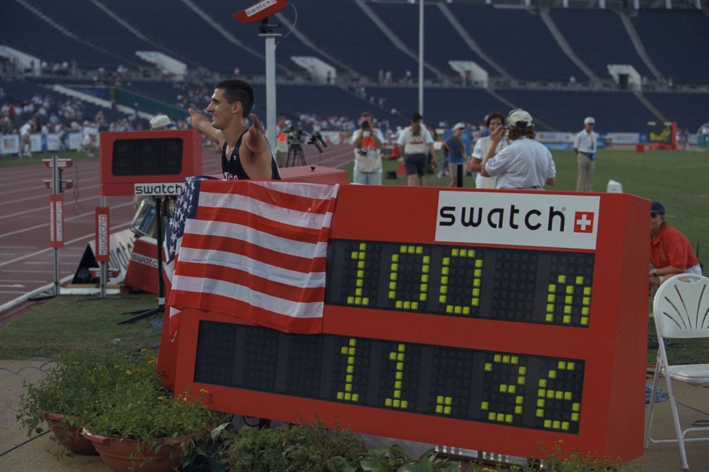 Tony Volpentest behind the trackside scoreboard reading 100m 11.36, a US flag draped over it