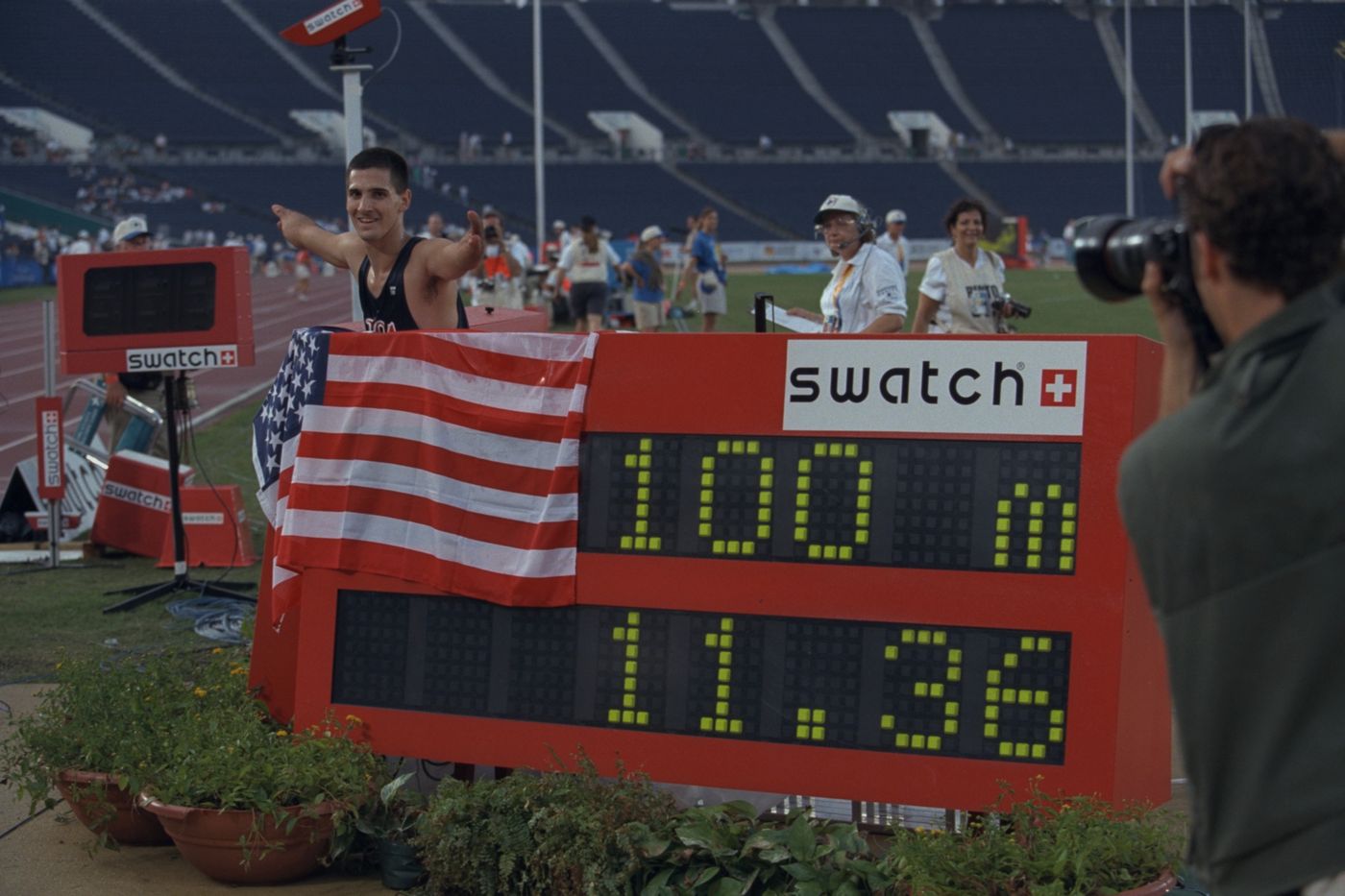 Tony Volpentest gesturing at the scoreboard reading 100m 11.36 as a photographer takes his picture