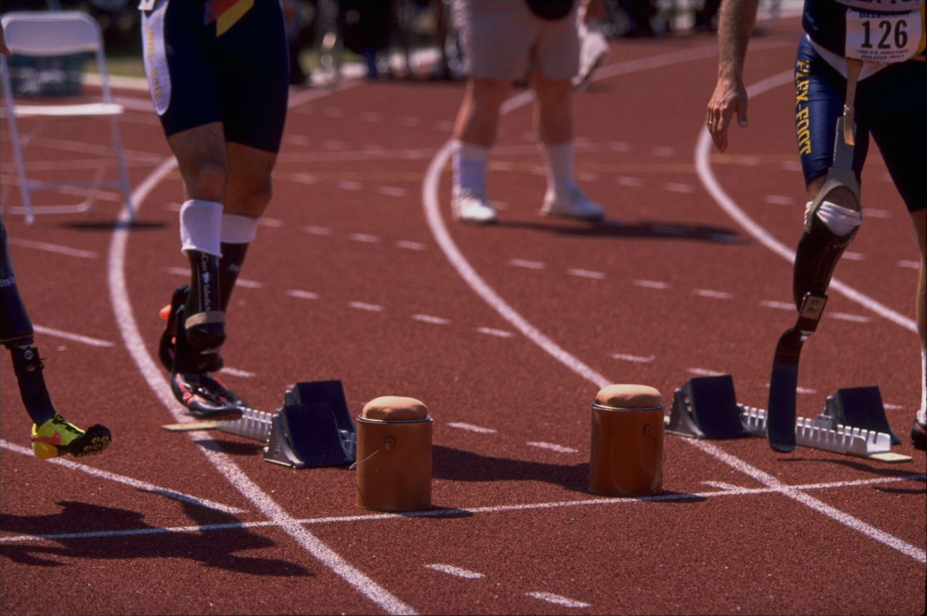 A close view of the start line: blocks, two padded starting supports, and sprinters&rsquo; legs and running prostheses as they step into position
