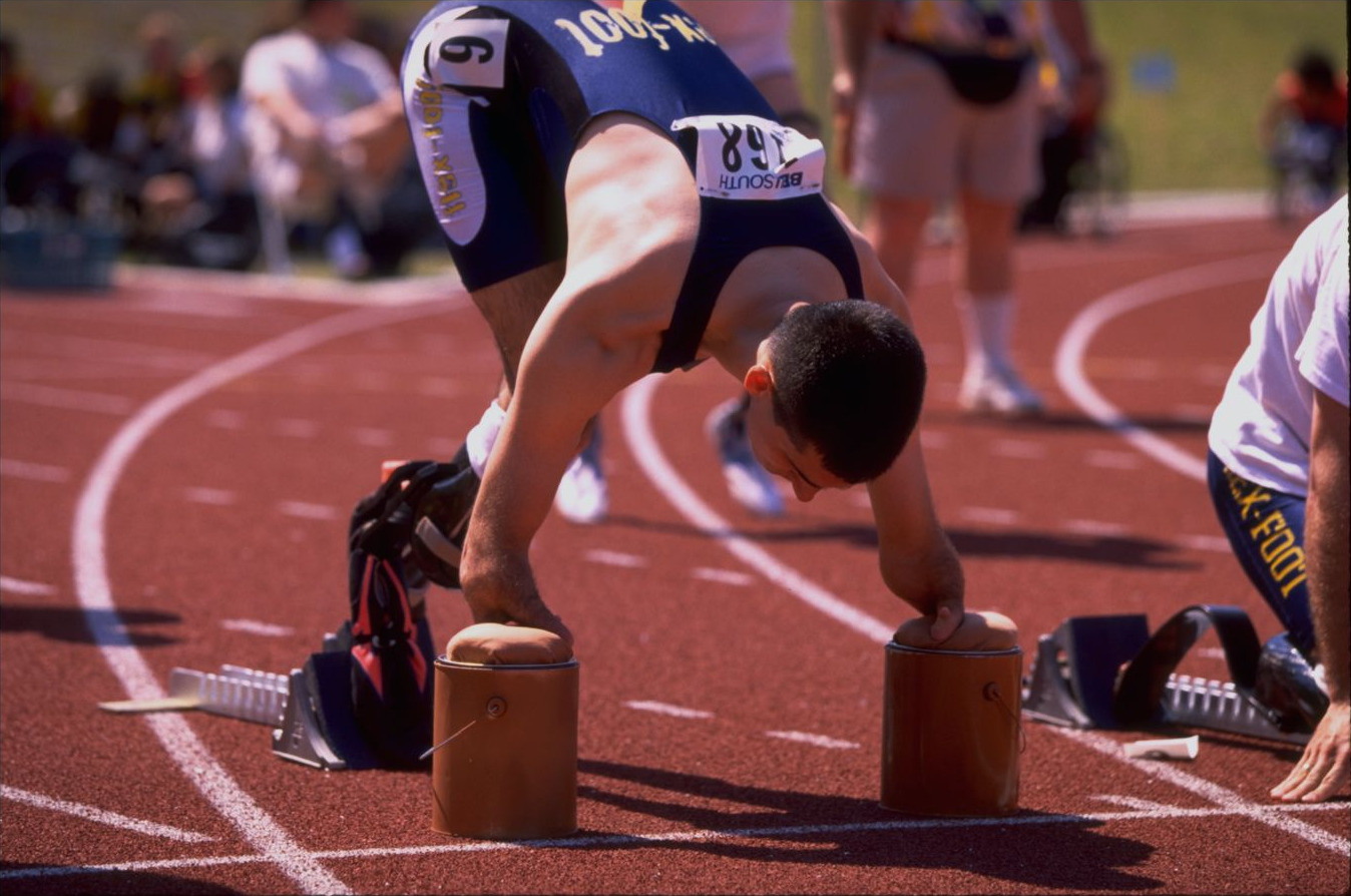 Tony Volpentest bent low over the starting supports, bib 168 and flex-foot singlet, blocks behind him