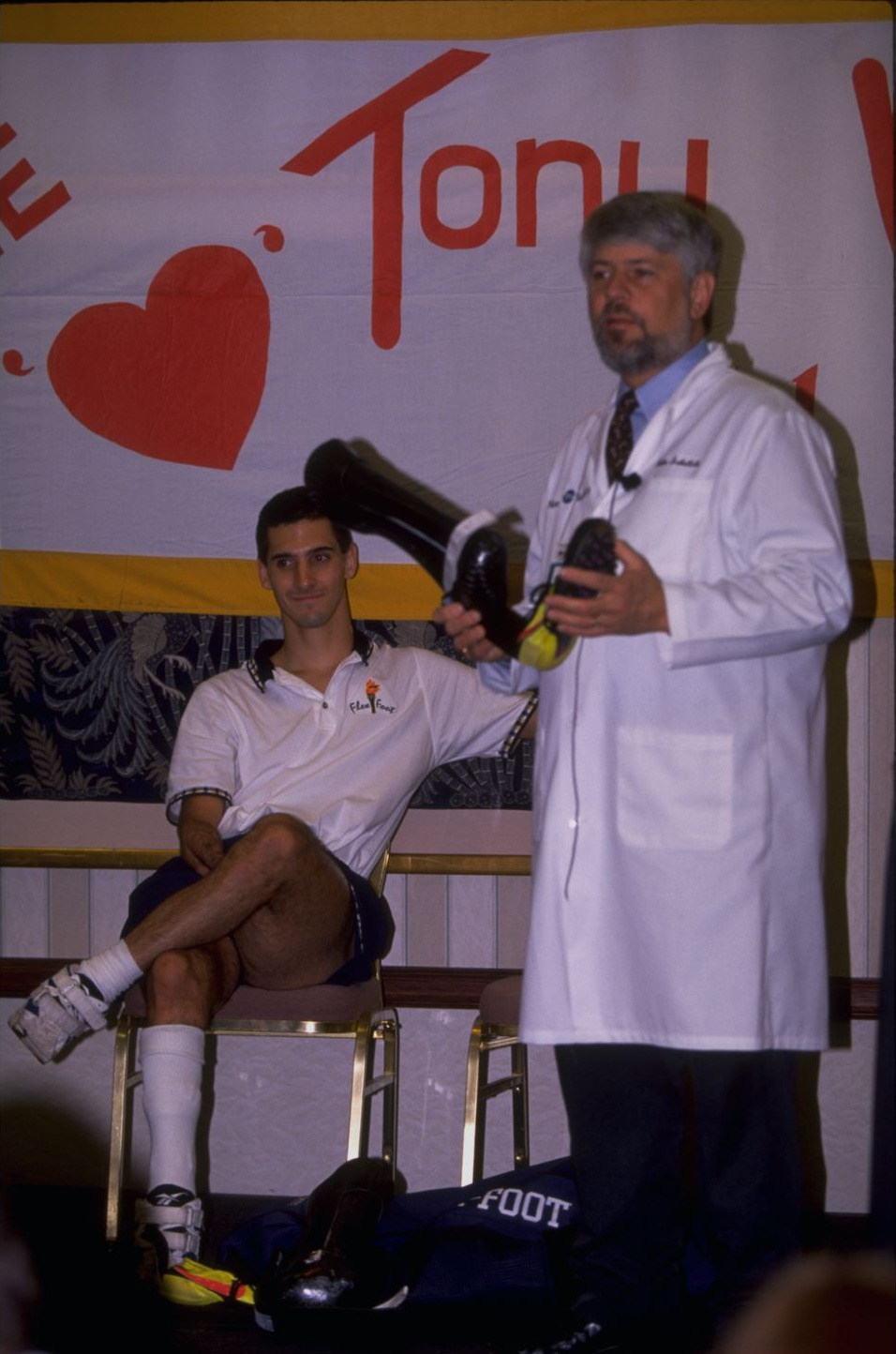 Tony Volpentest seated beside John Sabolich, who holds up a pair of carbon-fiber running prostheses