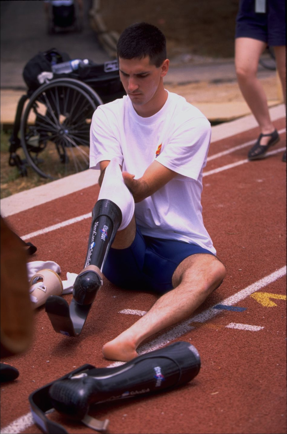 Tony Volpentest sitting on the track, pulling a sock over a carbon-fiber prosthesis